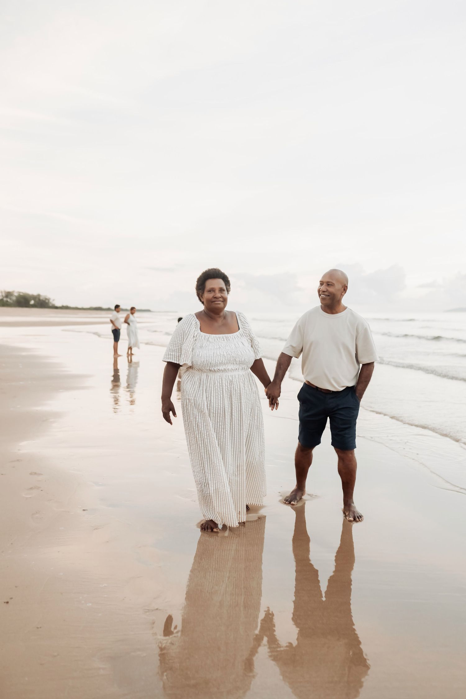 Couple takes romantic beach walk together in white dress and casual wear.