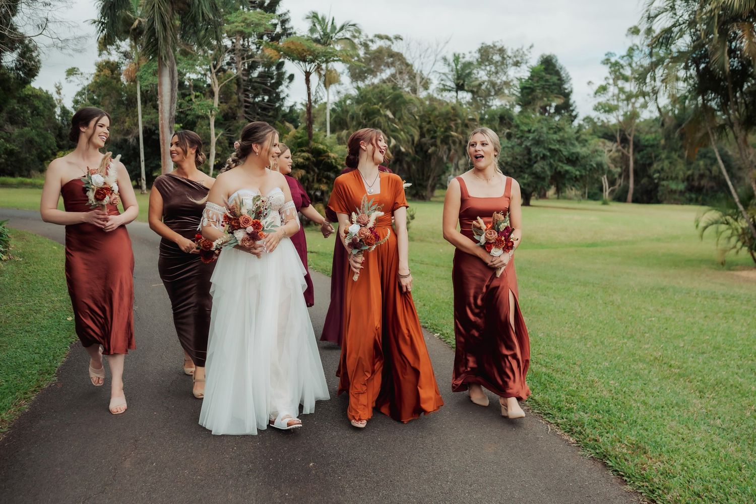 Bridal party in warm autumn colors walking together on an outdoor path.