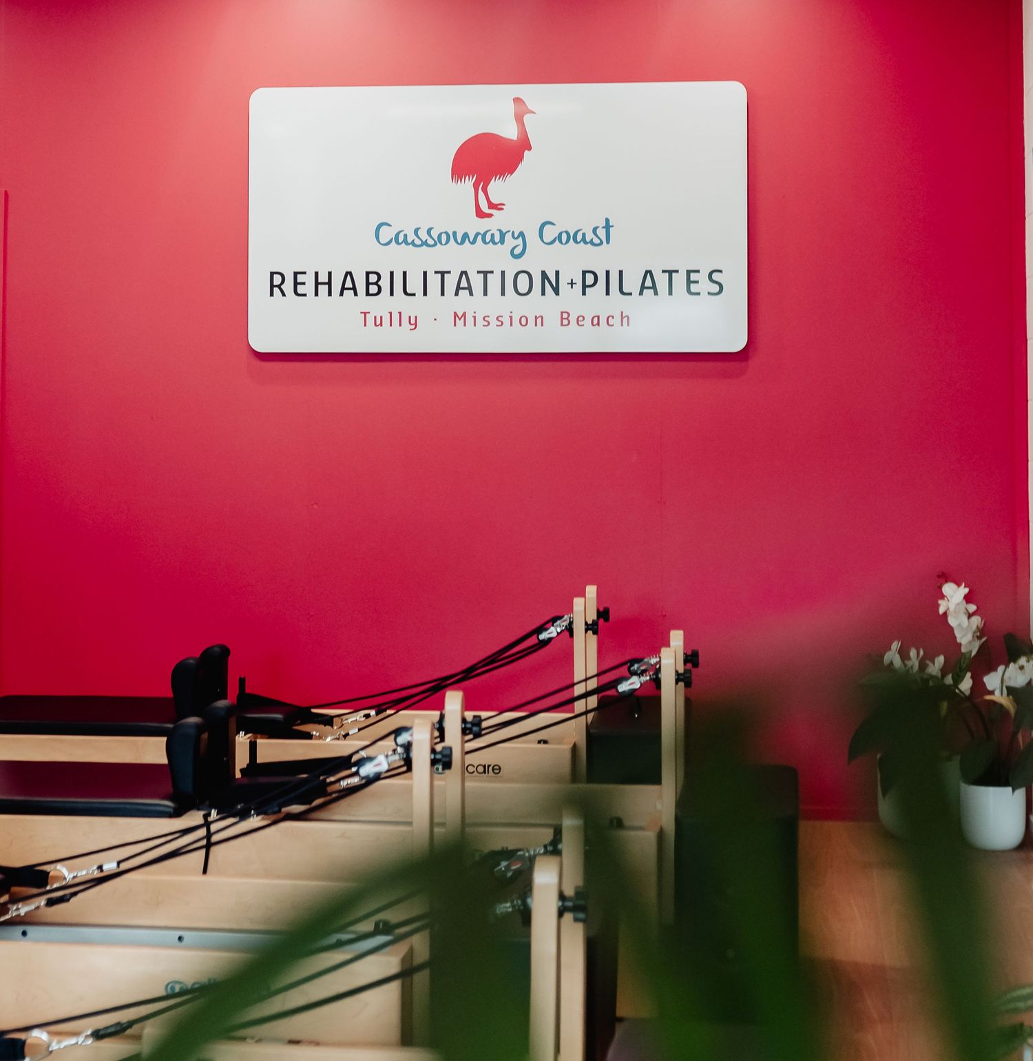 Cassowary Coast Rehabilitation Pilates studio interior with red walls, reformer equipment, and signage for Tully and Mission Beach.