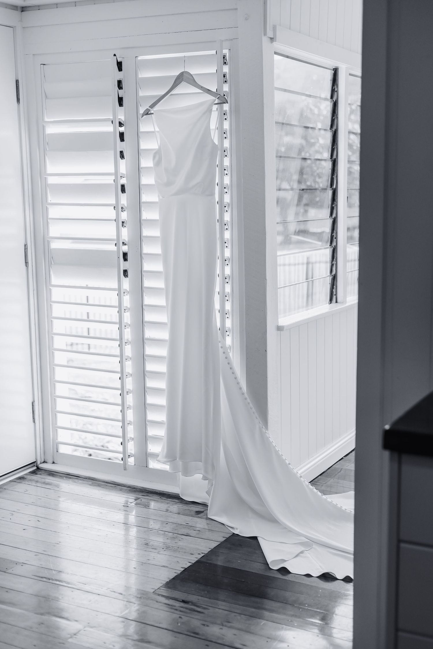Minimalist white room with shuttered windows and wooden floors creating dramatic lighting.