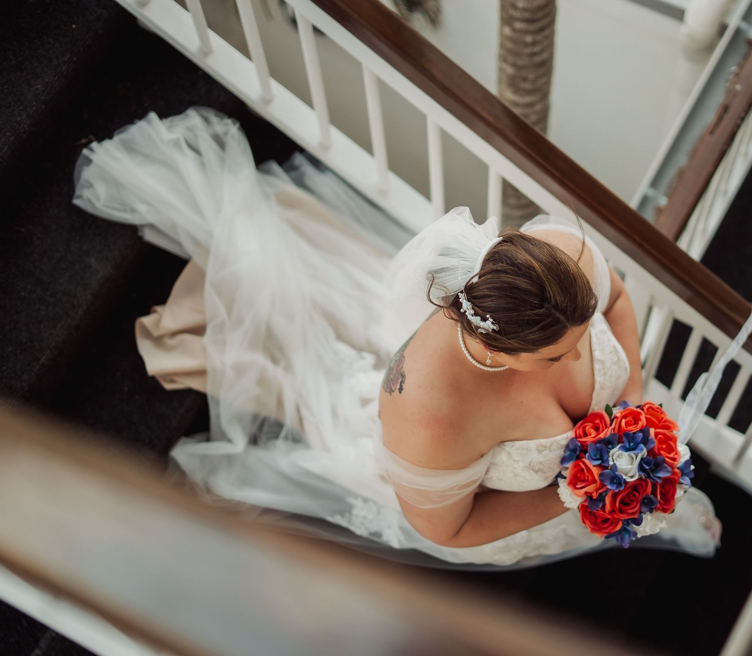 Wedding shoes and dress details arranged on white staircase with red and blue floral bouquet accents. Port Douglas