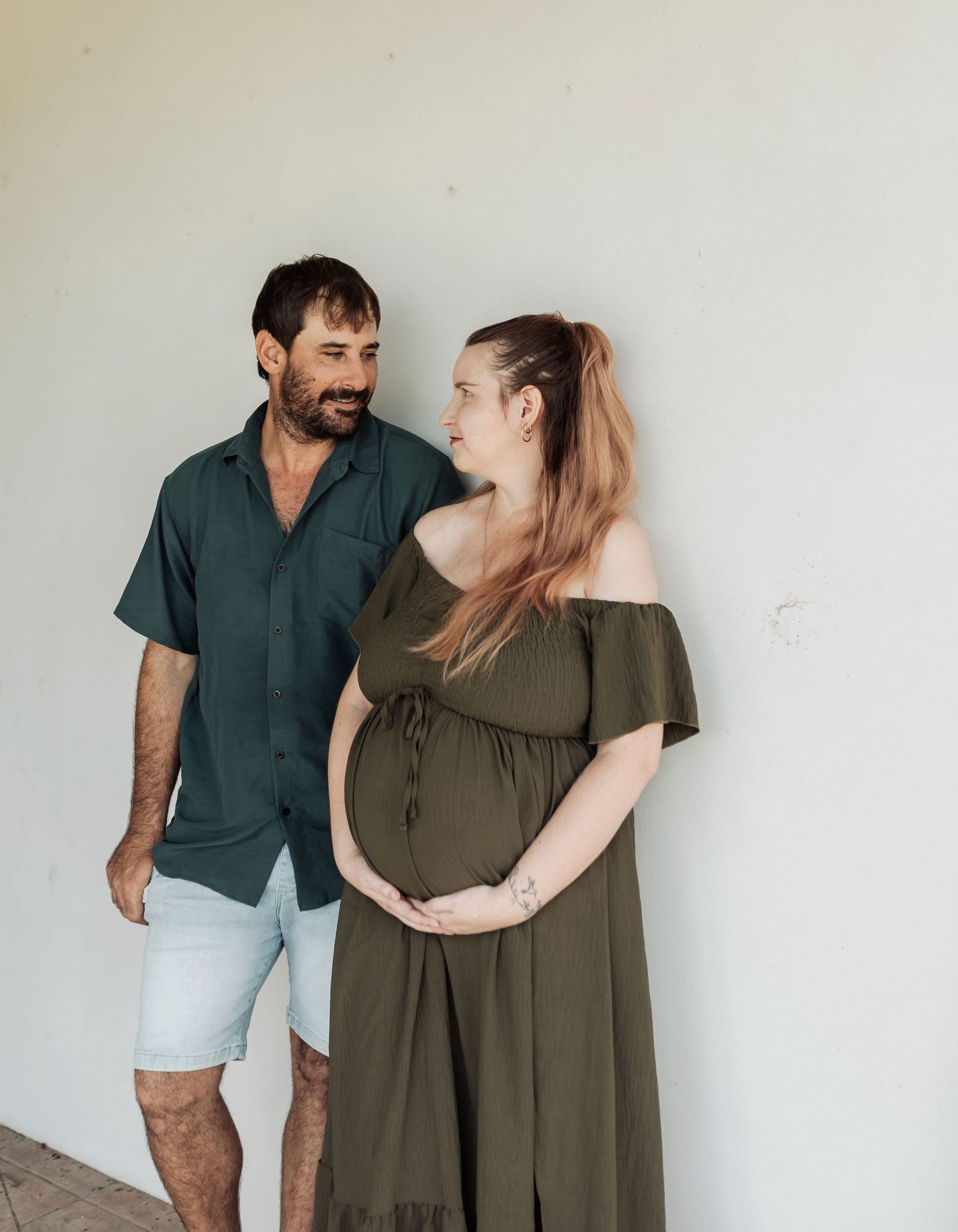 Expectant couple sharing a tender moment, woman in olive maternity dress cradling her baby bump.