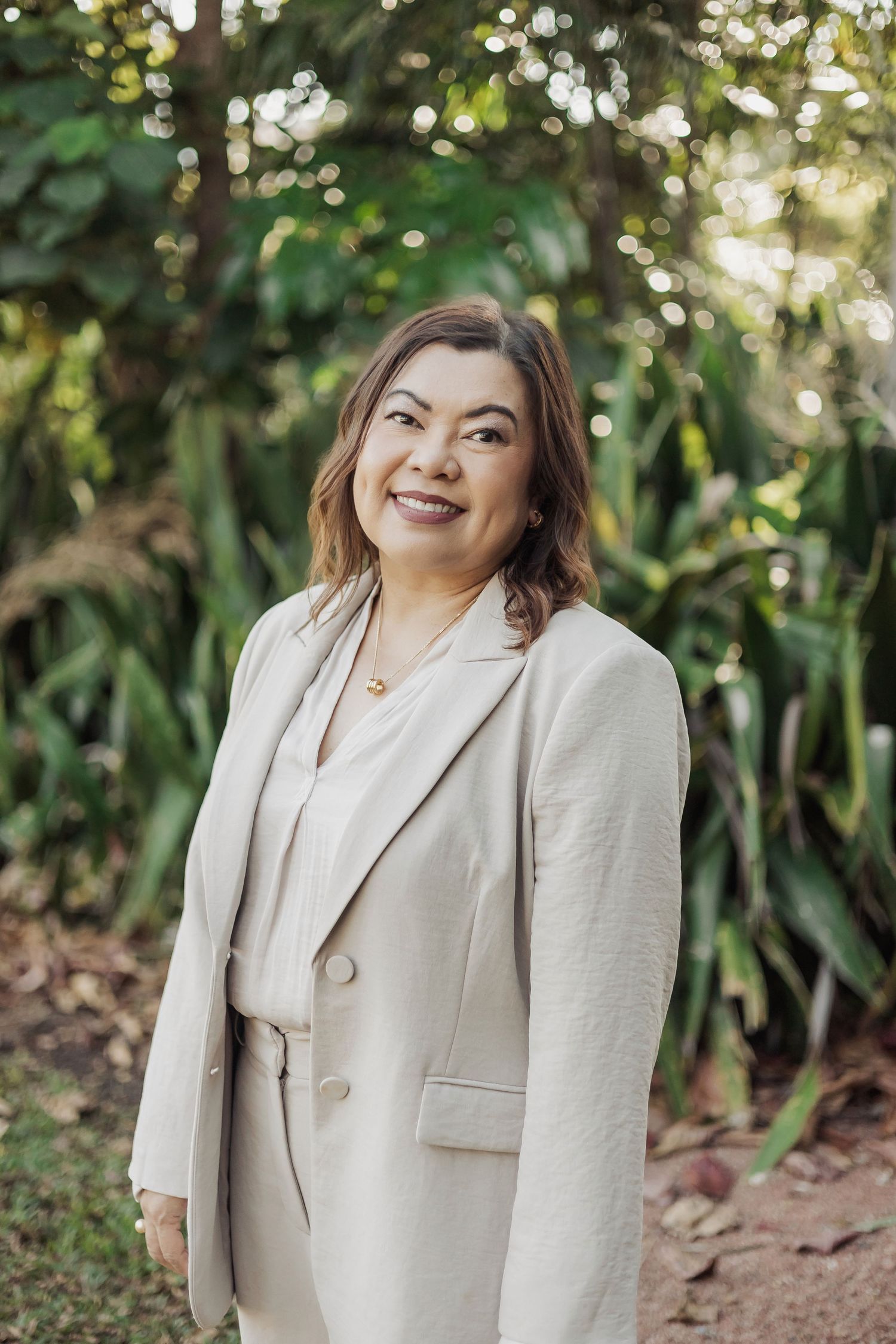 Woman in light colored business suit smiles warmly during outdoor photo session.