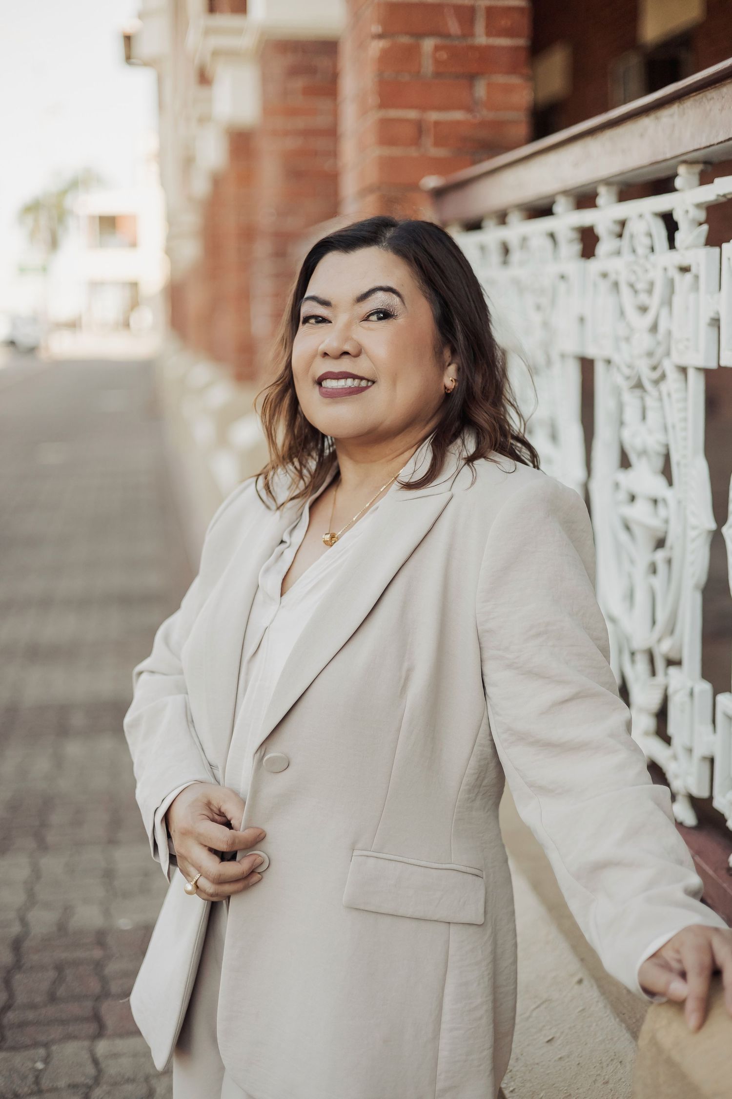 Professional headshots of woman in beige blazer against brick wall background.