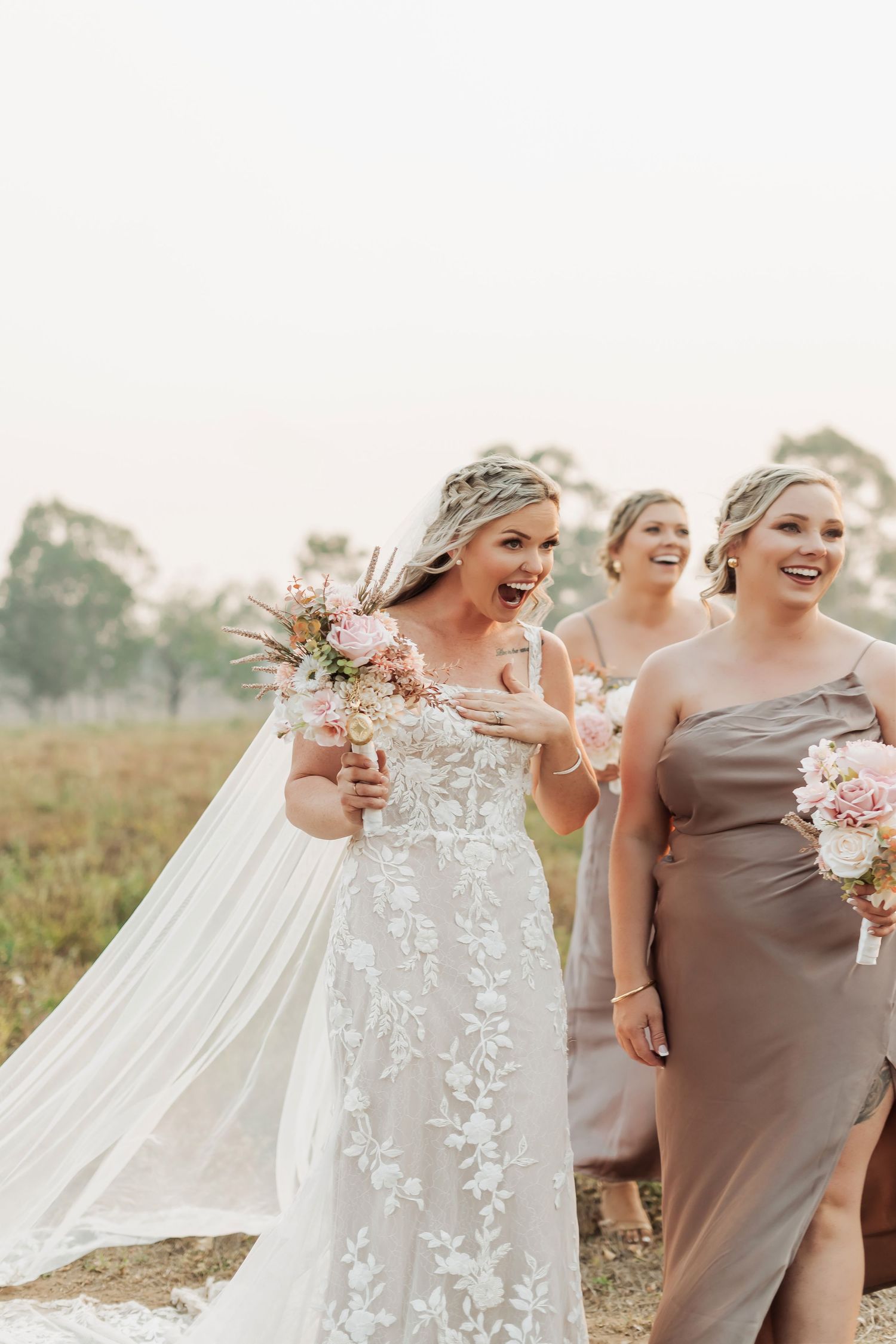 Bridesmaids in neutral dresses laughing together during an outdoor wedding celebration.