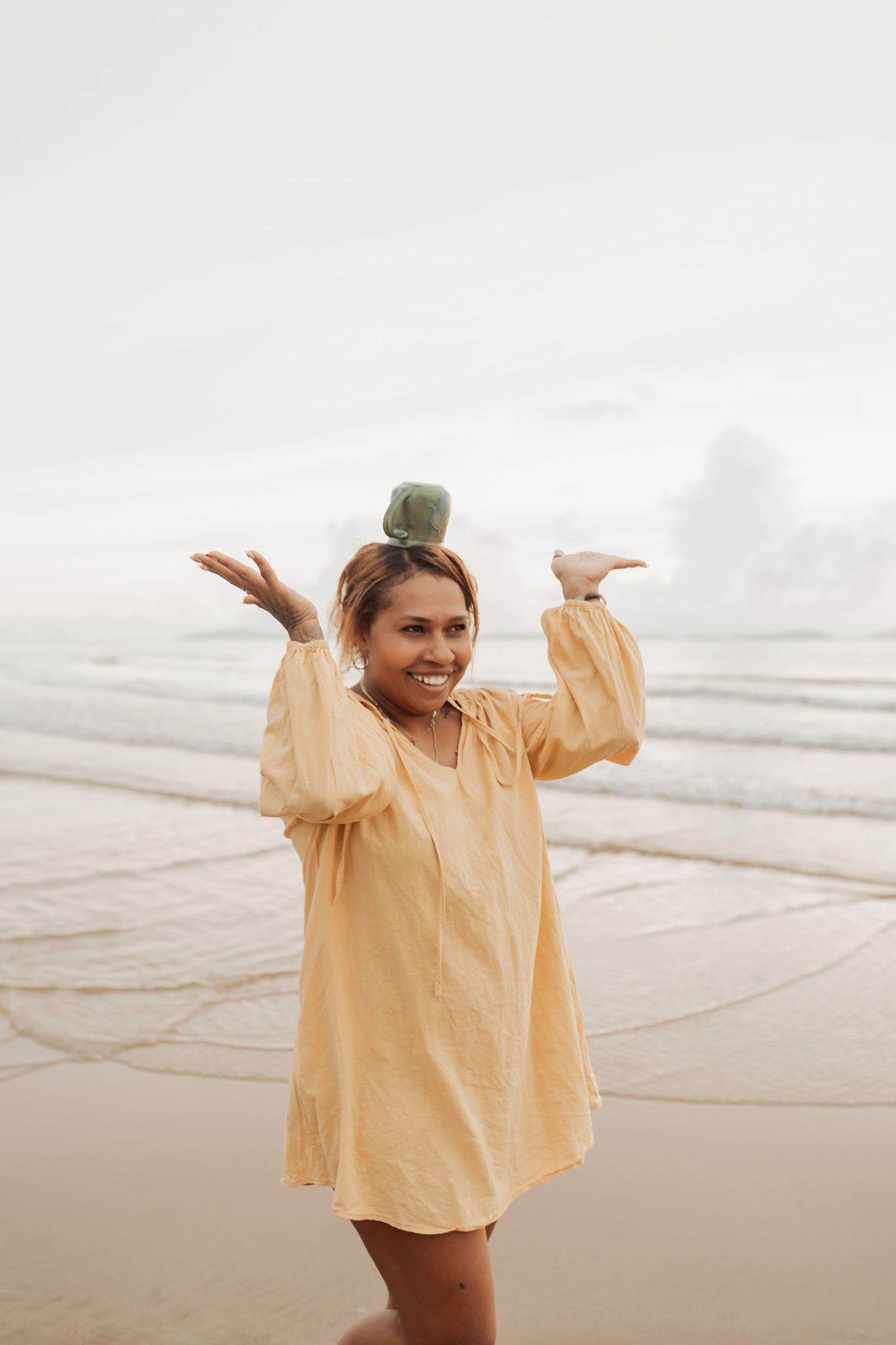 Person in yellow flowing top dances joyfully on a misty beach at sunset.