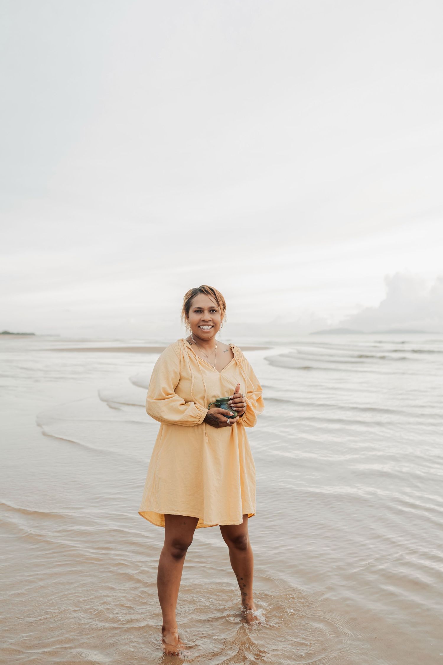 Beachside photography session with person in yellow shirt standing in shallow water.