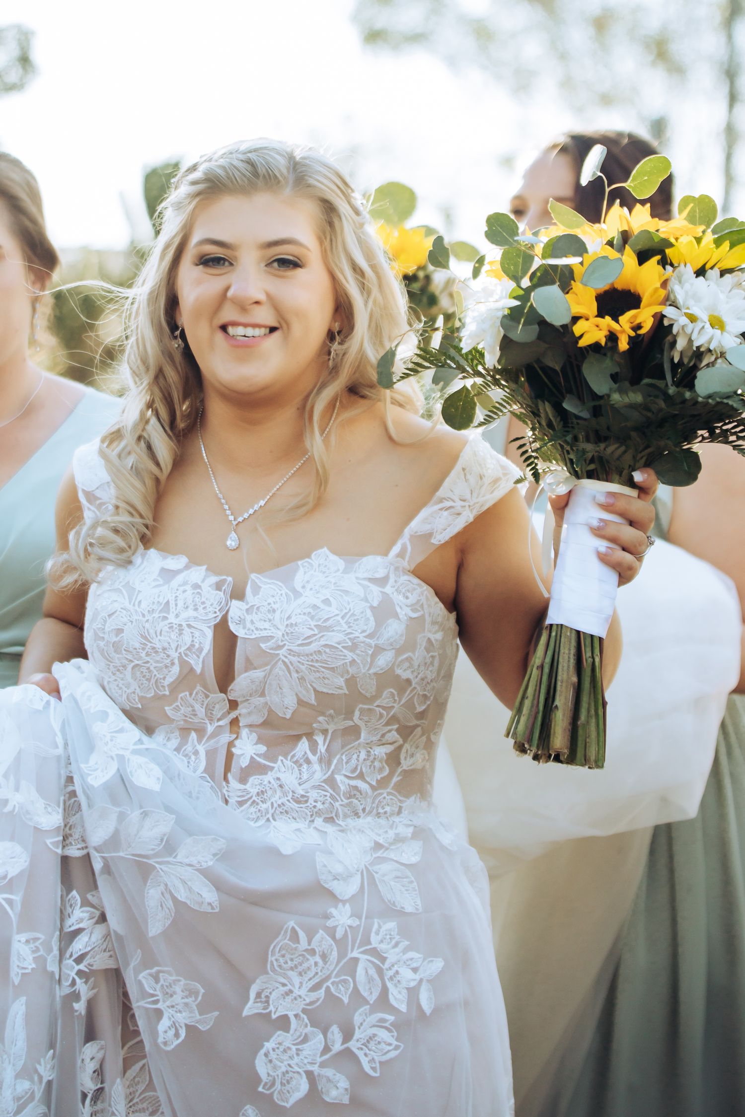 Bride in lace dress holds a vibrant sunflower and white flower bouquet. Long Horns Charters Towers