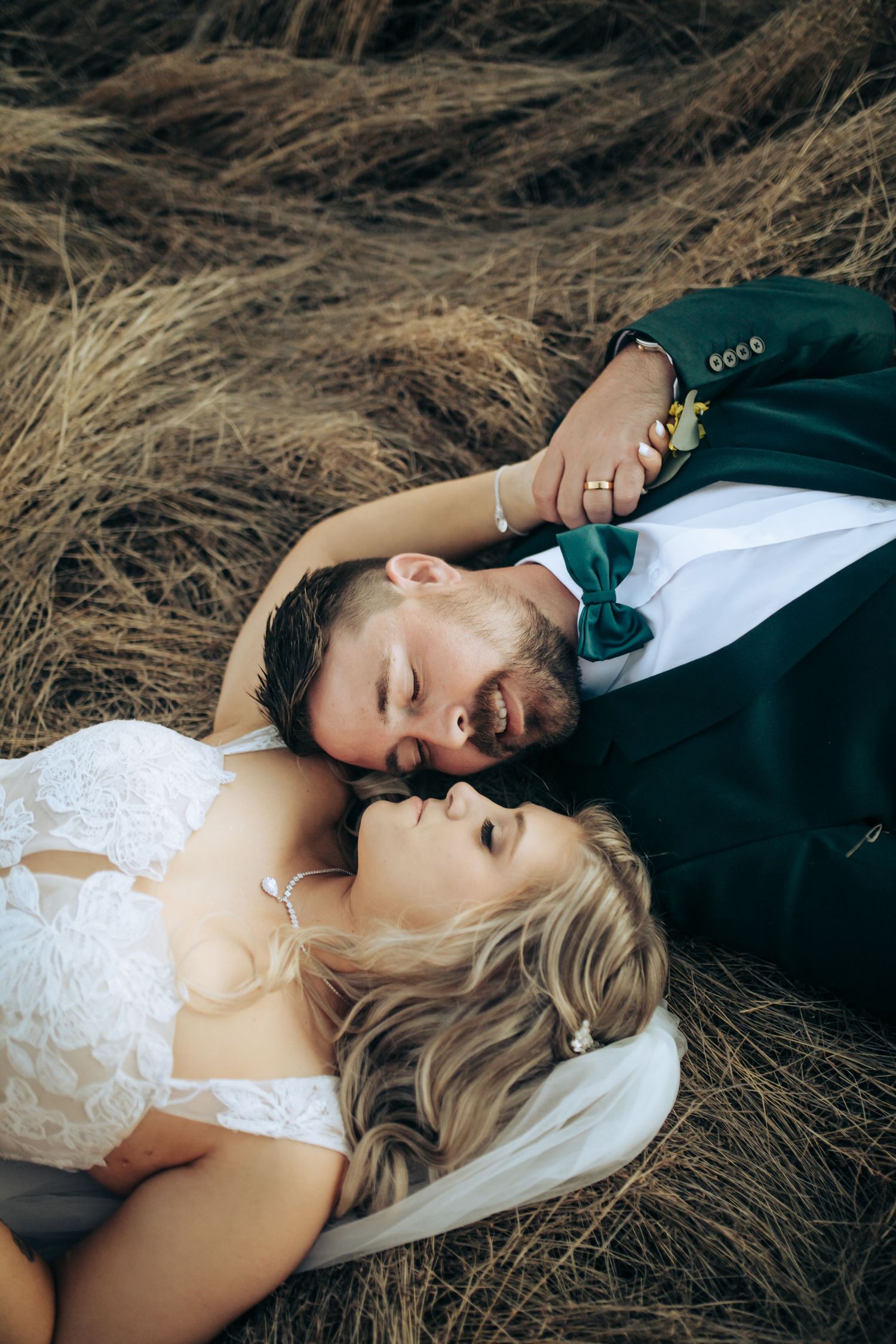 Couple in wedding attire lying in tall grass during a romantic outdoor photoshoot. Long Horns Charters Towers