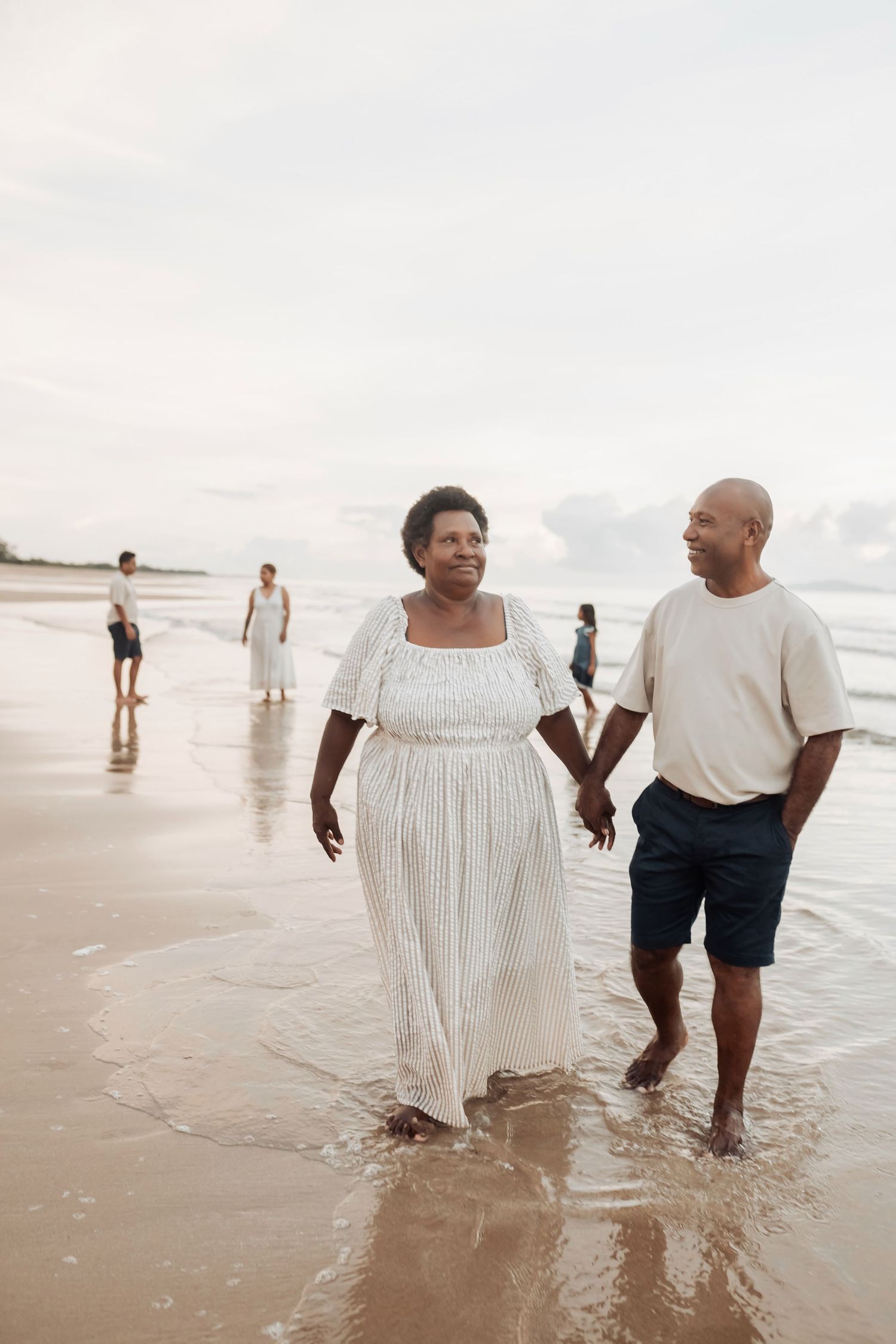 Two people wading in shallow ocean water during a beach photoshoot.