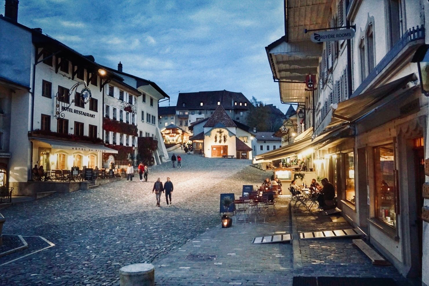 Evening panorama of a charming European village street with illuminated shops and historic buildings.