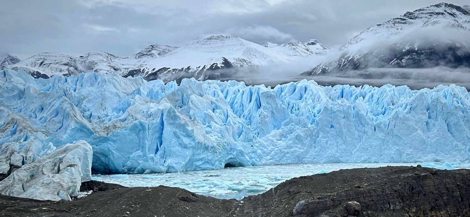 Massive blue glacier wall stretches across snowy mountain landscape in Patagonia's Los Glaciares National Park.