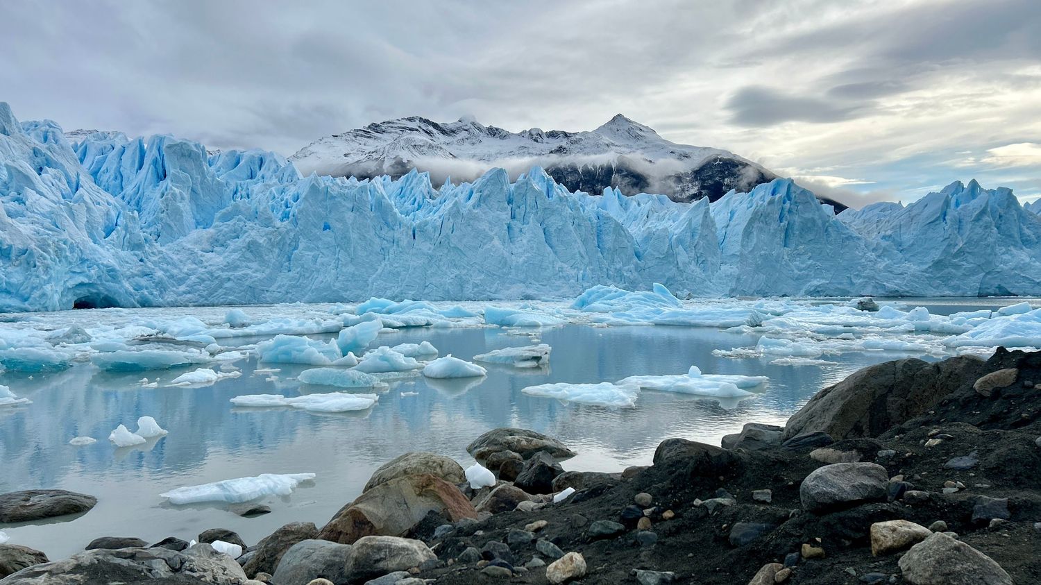 Panoramic view of massive blue glaciers and snow-capped mountains reflecting in calm arctic waters at sunset.