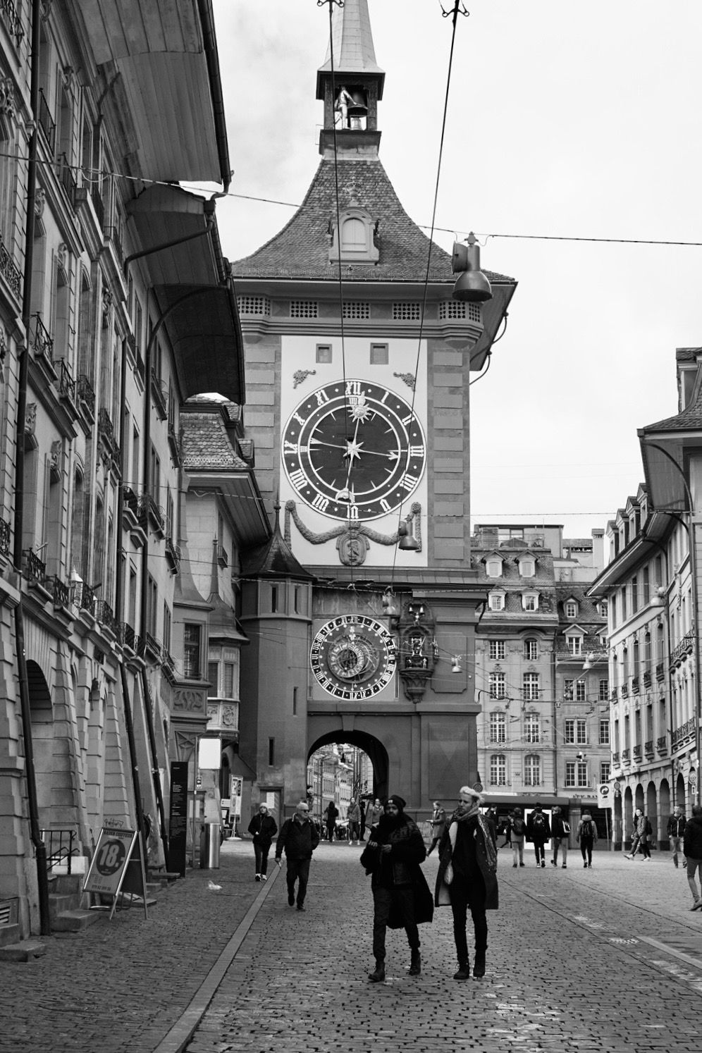Historic clock tower and cobblestone street in Bern's old town captured in black and white.