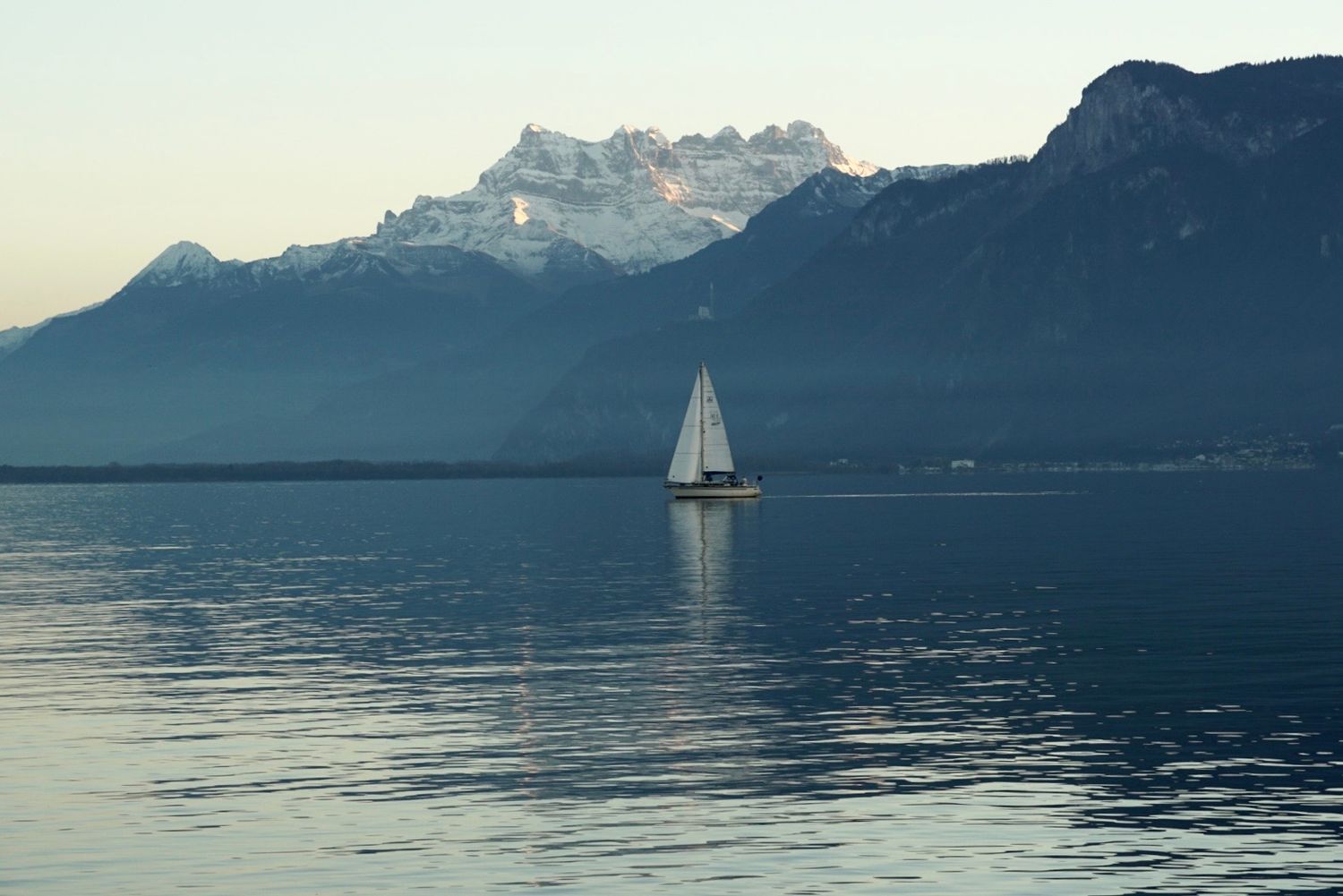 Scenic mountain lake view with sailboat silhouettes gliding across calm waters during sunset in the Alps.