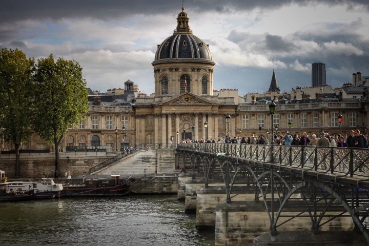 Panoramic view of European architecture with domed buildings and waterfront under dramatic cloudy sky.