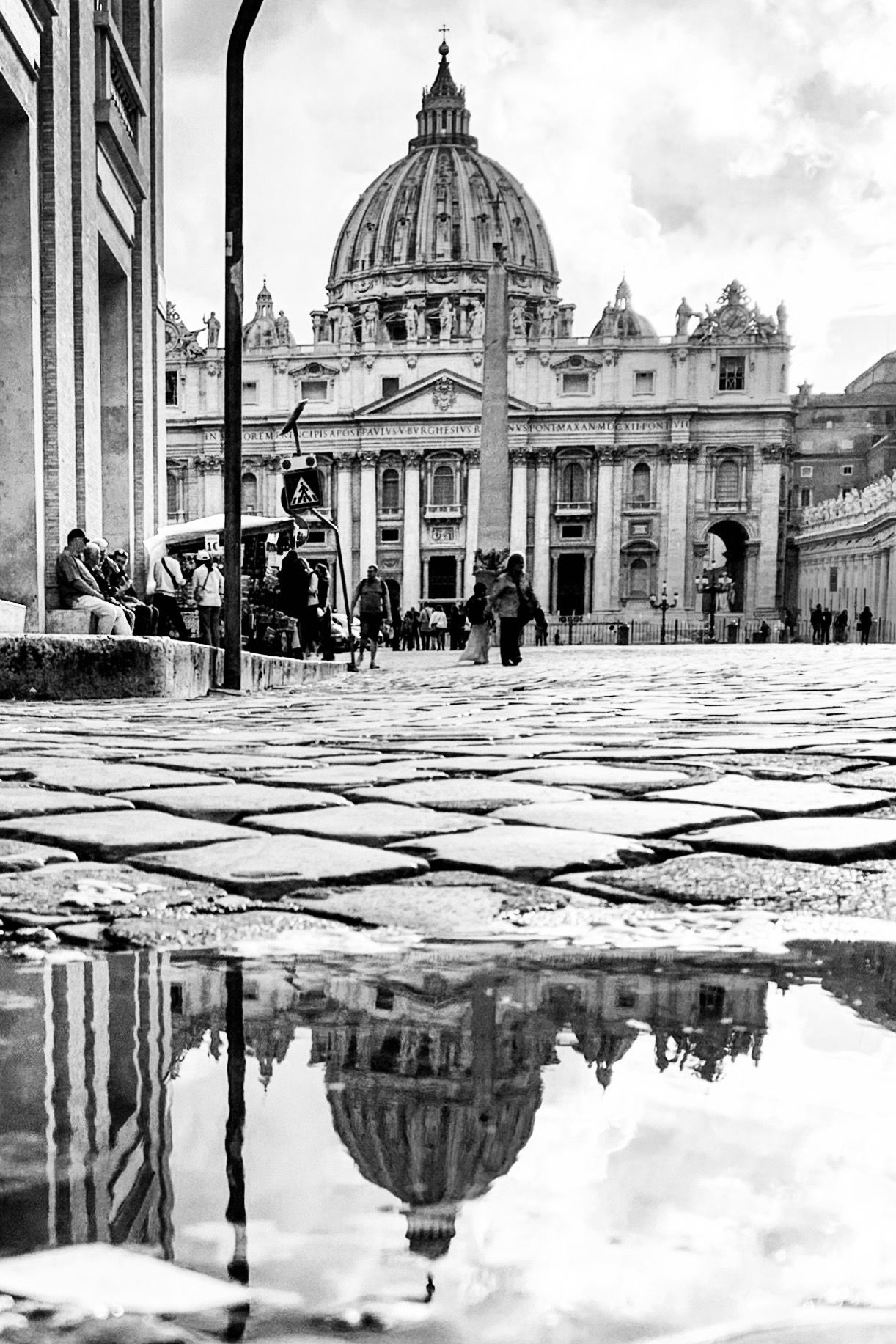 Dramatic reflections of St. Peter's Basilica in Vatican City captured in puddles on the square's wet pavement.
