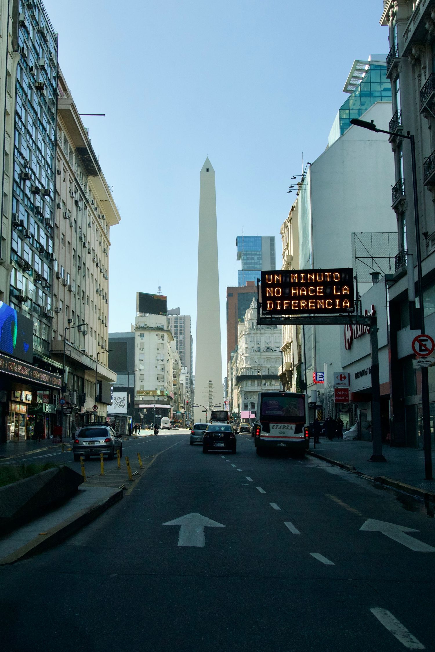 Urban street view showing the iconic Buenos Aires Obelisk from multiple angles with traffic signs in the foreground.