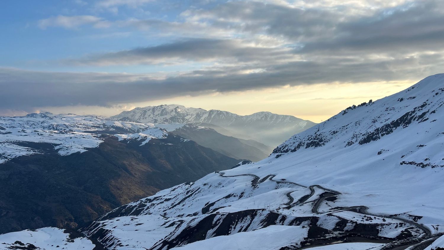 Snow-covered mountain peaks under dramatic cloudy skies during winter.