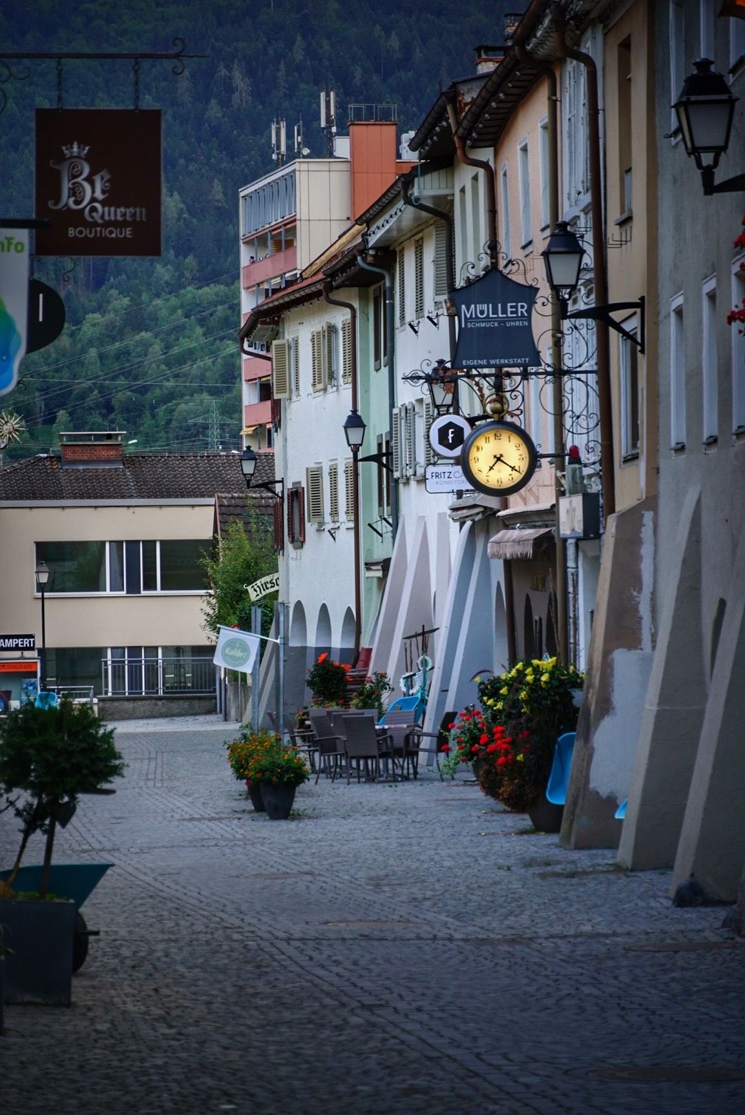 Quaint cobblestone shopping street with traditional storefronts and hanging flower baskets in a European town.
