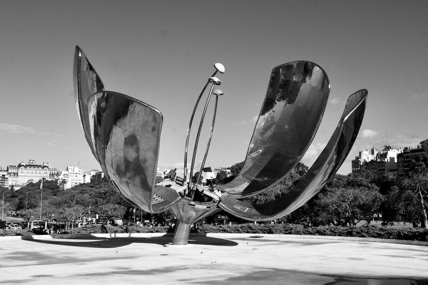 Curved metal sculptures reflect sunlight against a cityscape backdrop in an artistic installation.