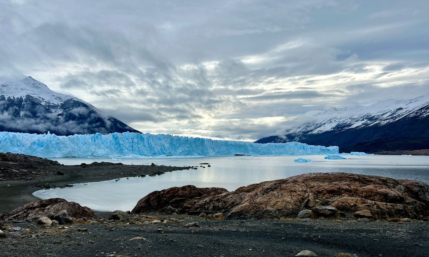 Panoramic view of glaciers and snow-capped mountains against a moody cloudy sky.