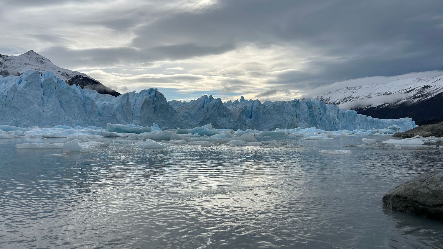 Panoramic view of massive glaciers and icebergs floating in calm arctic waters under a cloudy sky.