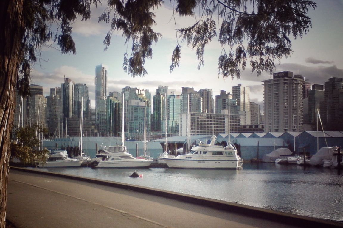Panoramic cityscape view of modern skyscrapers and harbor across calm waters during overcast day.