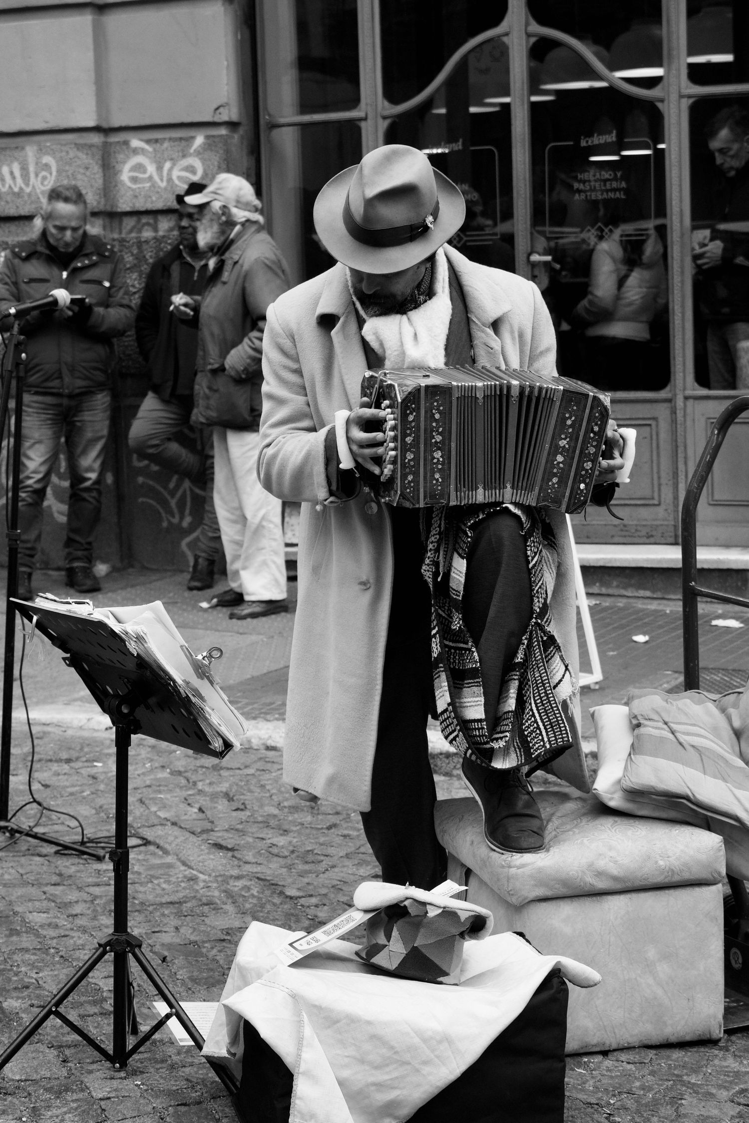 Street performer playing accordion on cobblestone plaza with music stand and white cloth.