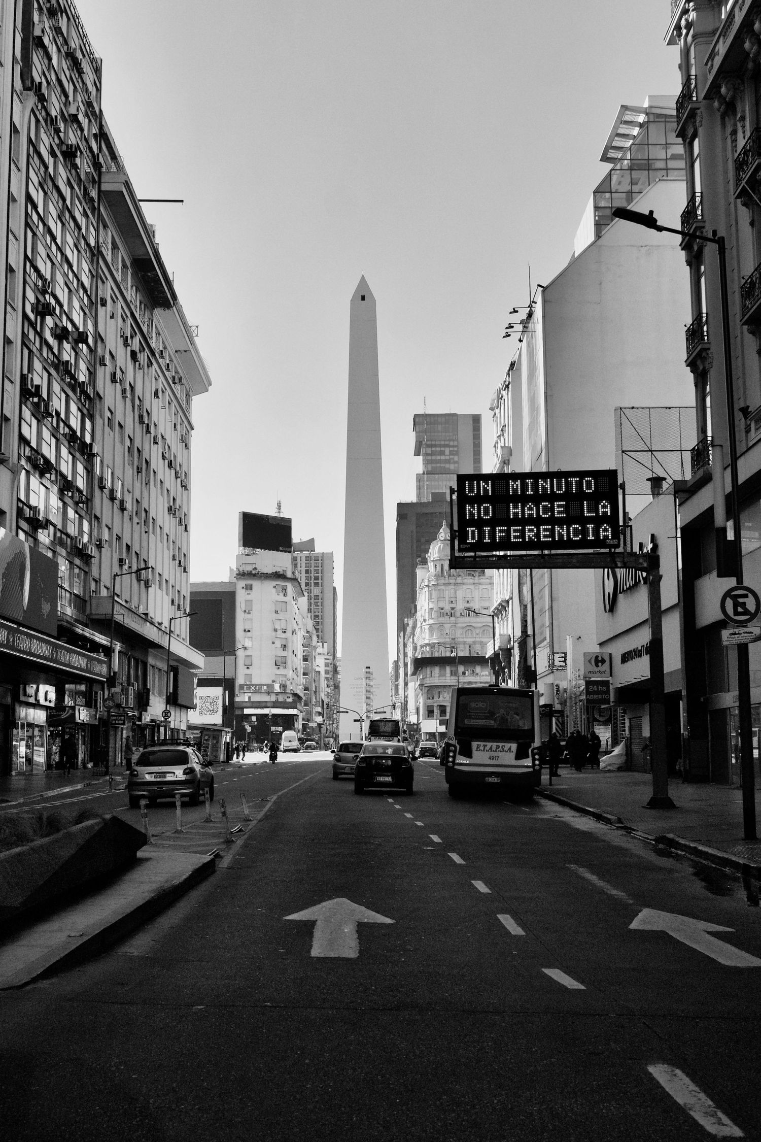 Black and white urban street scene with obelisk monument visible in the distance.