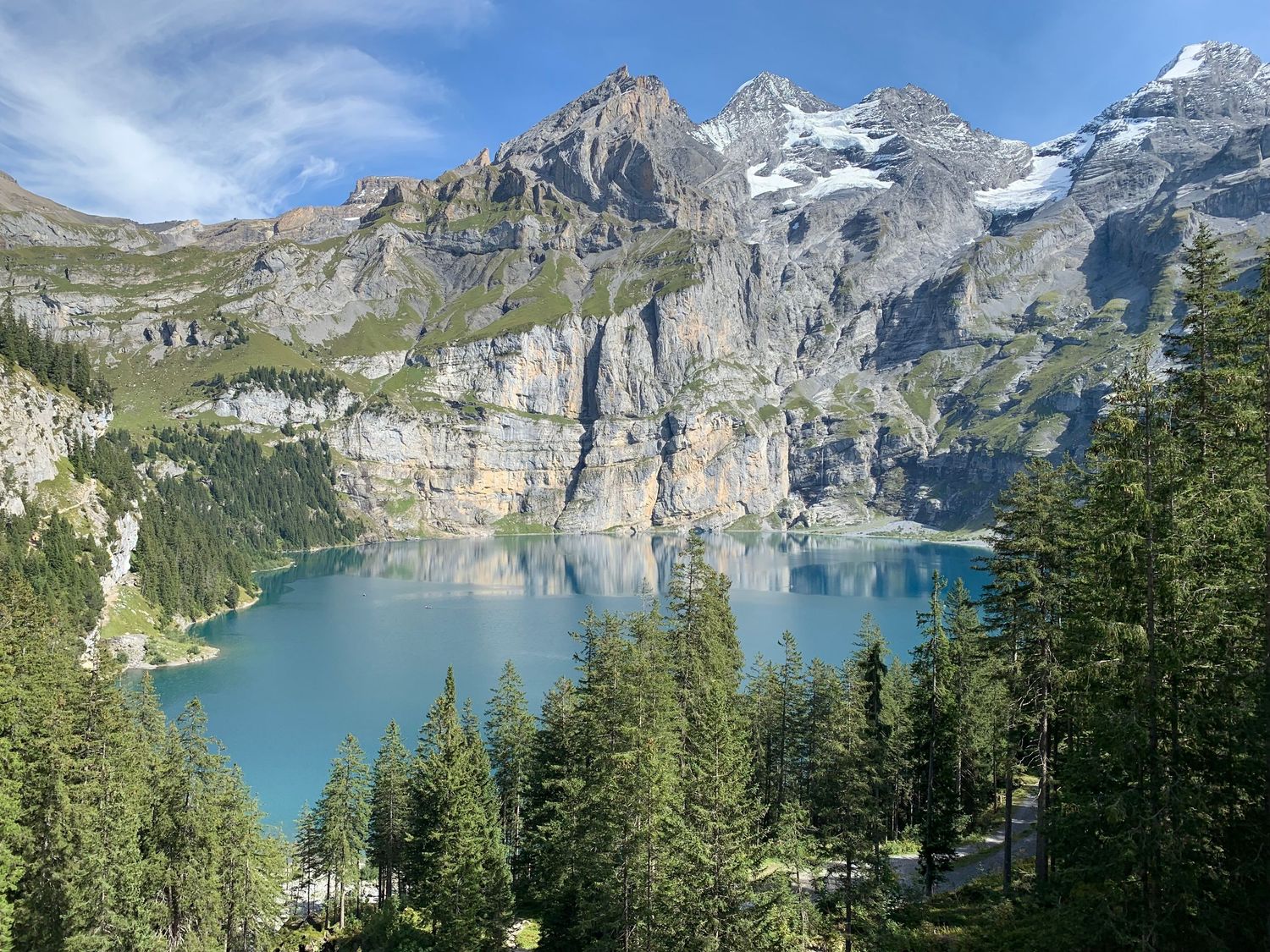 Panoramic view of snow-capped mountains surrounding turquoise alpine lake Oeschinensee in Switzerland.