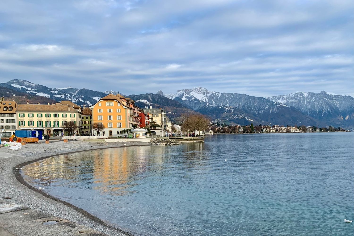 Panoramic view of a coastal town with colorful buildings and snow-capped mountains in the background.