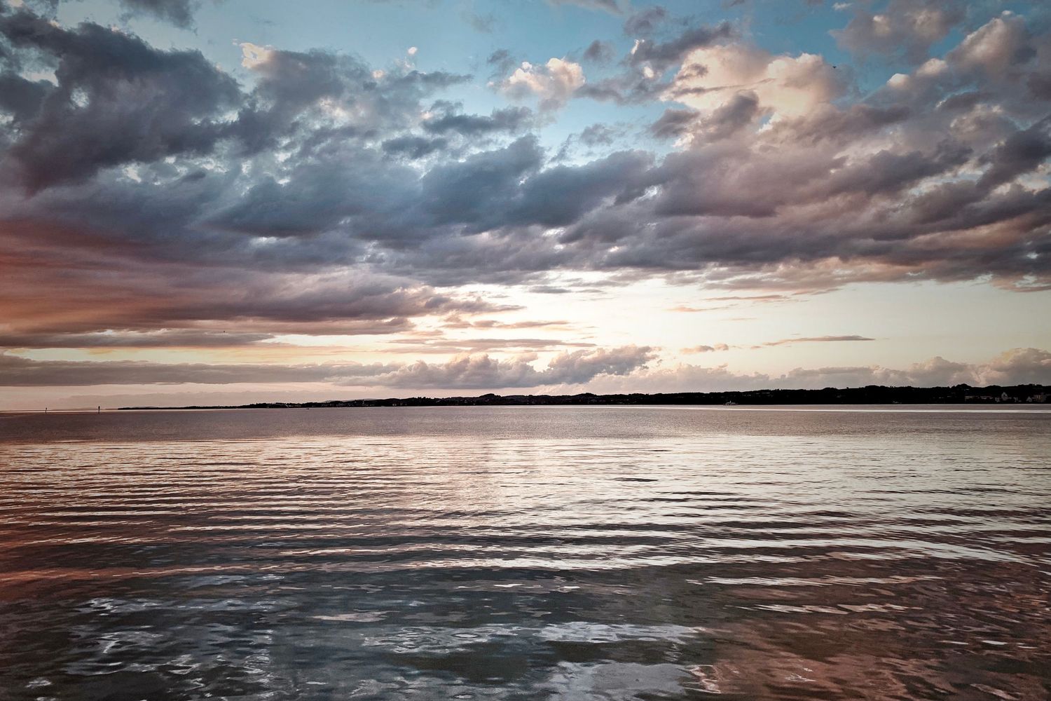 Dramatic sunset over a vast ocean with colorful clouds reflecting on the rippling water surface.