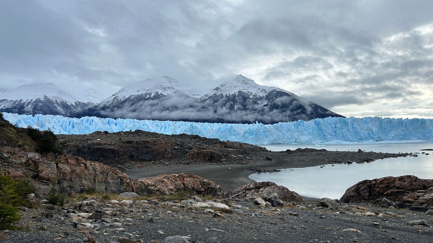 Wide panorama of rugged mountain terrain with snow patches and rocky outcrops under overcast skies.