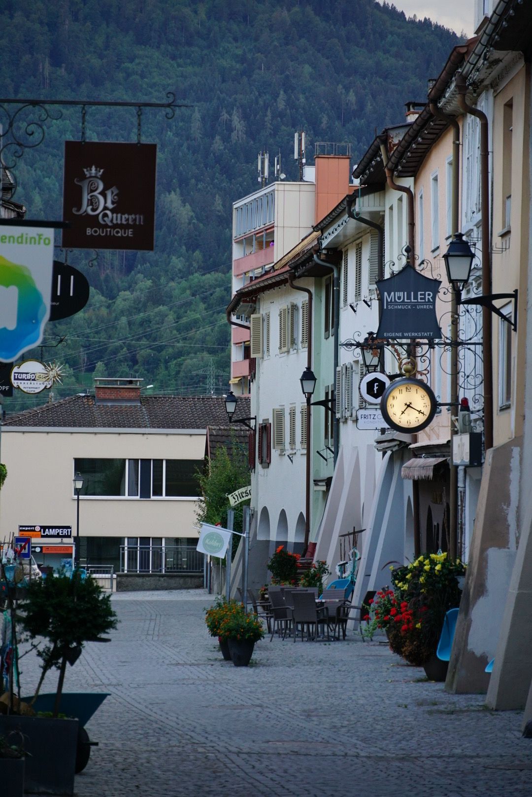 Charming European village street with traditional white buildings and mountain backdrop at dusk.