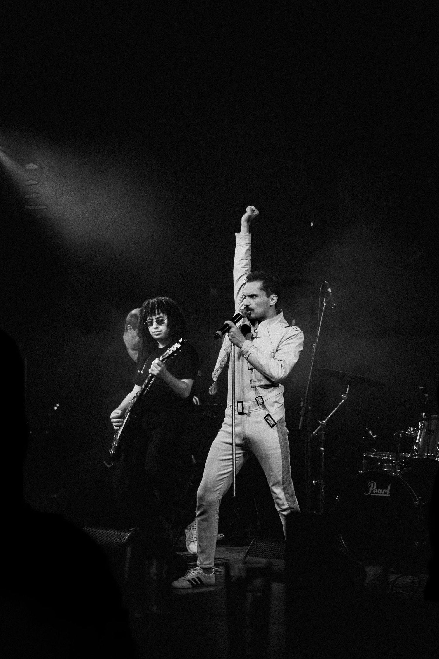Vocalista ergue o punho no palco ao lado do guitarrista, em fotografia em preto e branco.