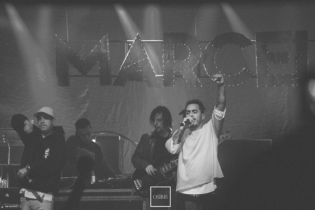 Cantor se apresenta com músicos ao fundo, em fotografia em preto e branco.