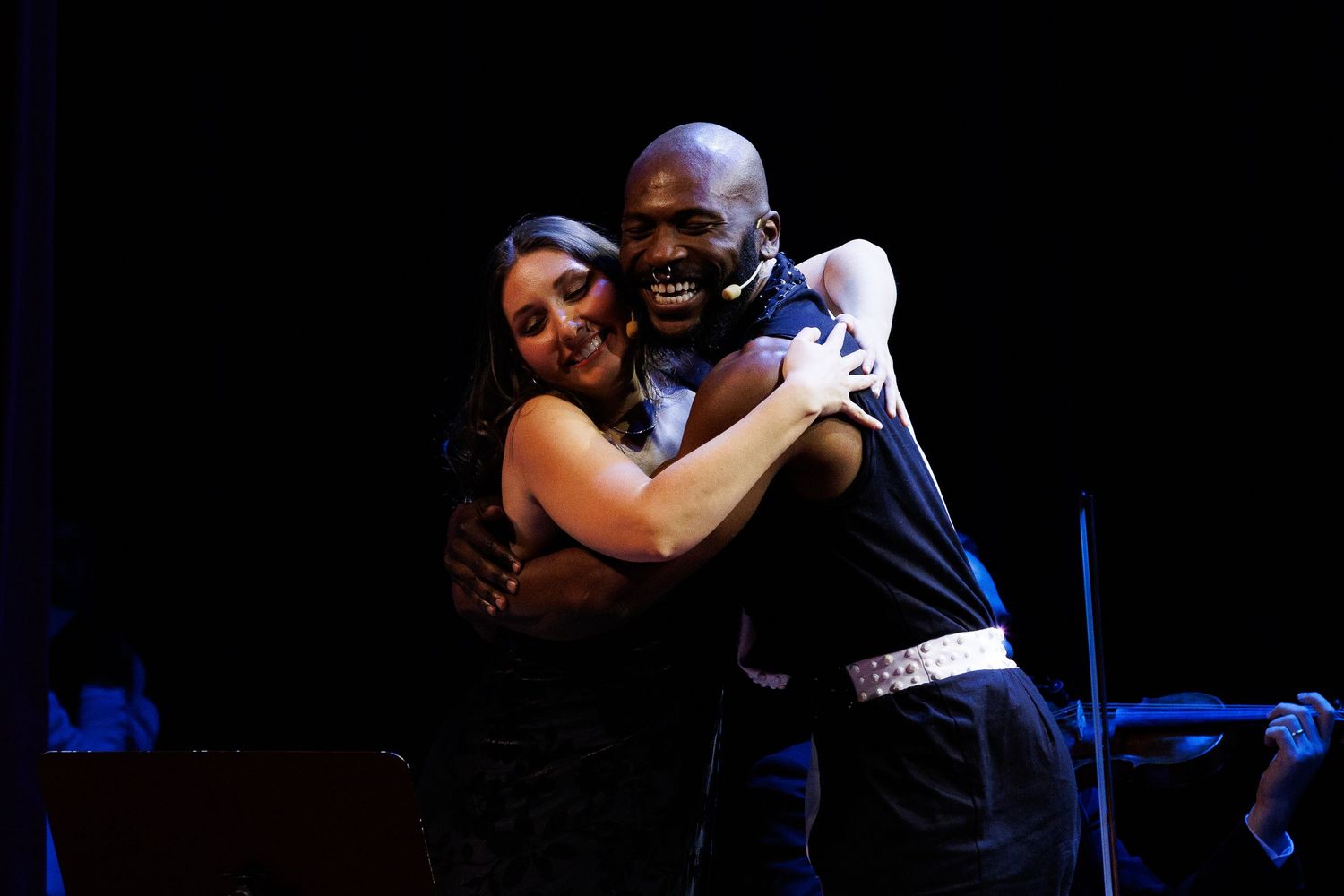 Dois intérpretes se abraçam sorrindo no palco.
