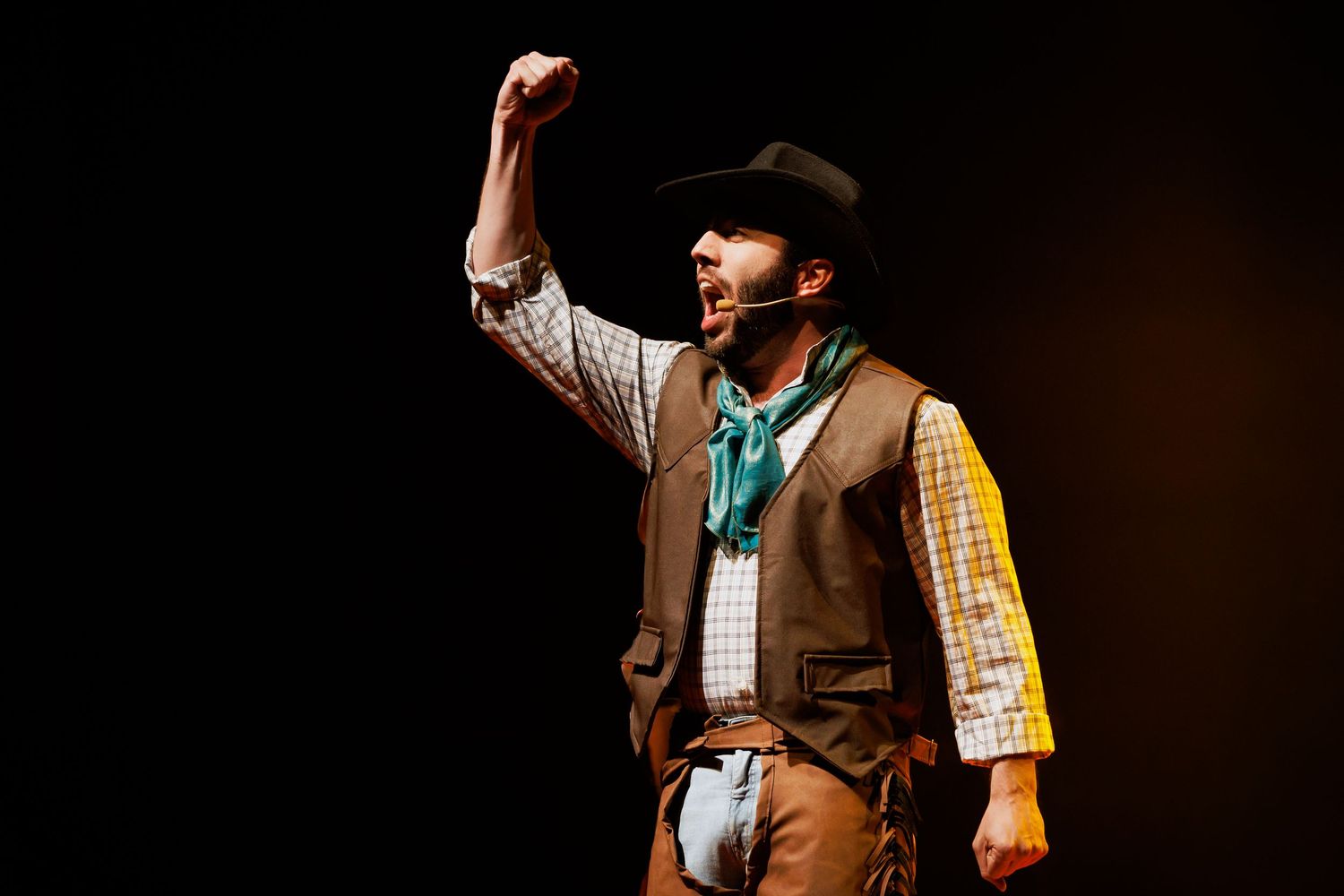 Intérprete de chapéu de cowboy e colete ergue o punho no palco.