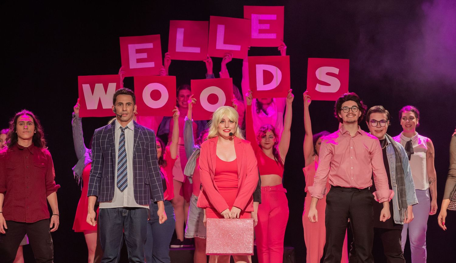 Elenco de Legalmente Loira ergue placas cor-de-rosa formando o nome Elle Woods.