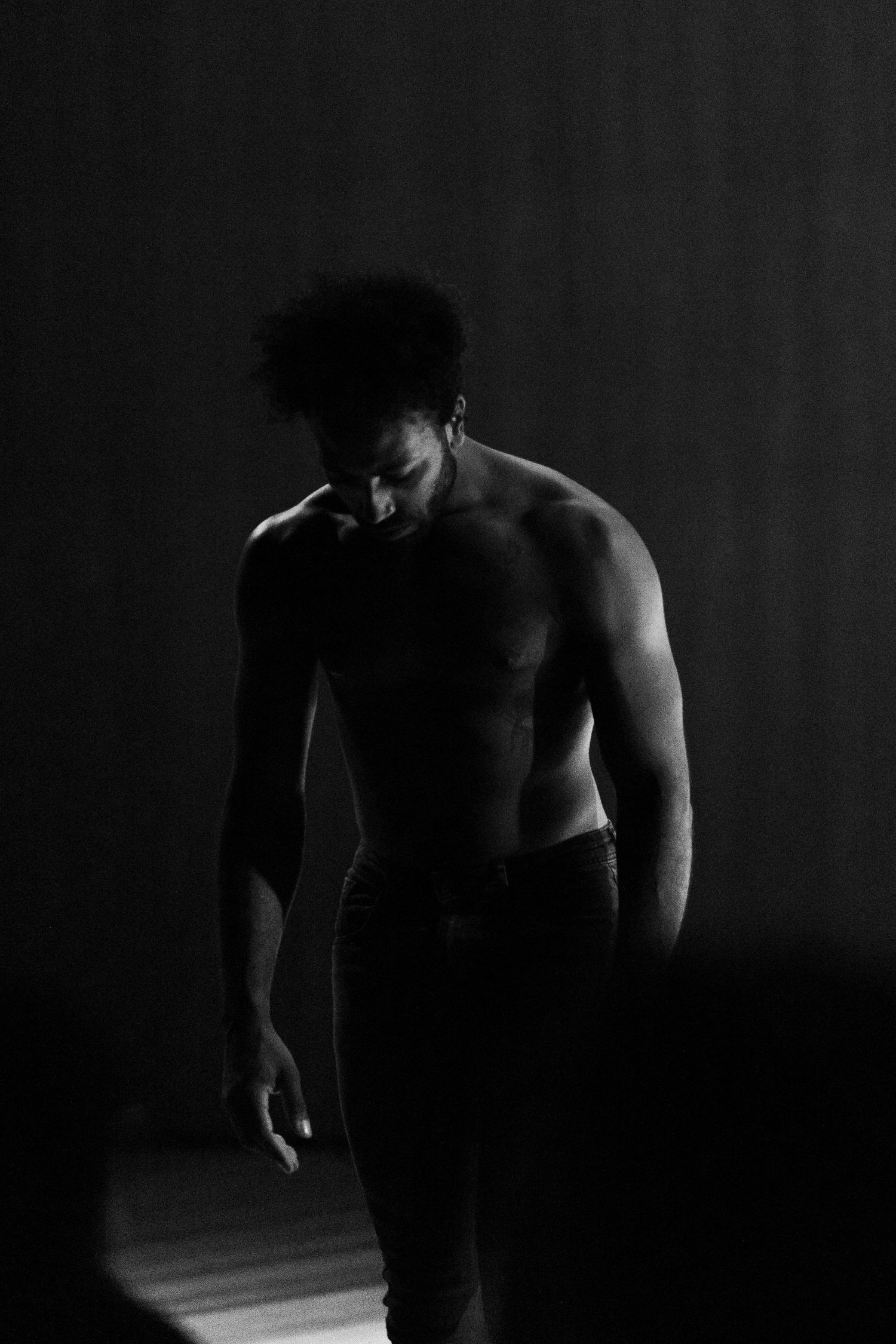 Intérprete sem camisa caminha pelo palco com a mão no rosto, em fotografia em preto e branco.