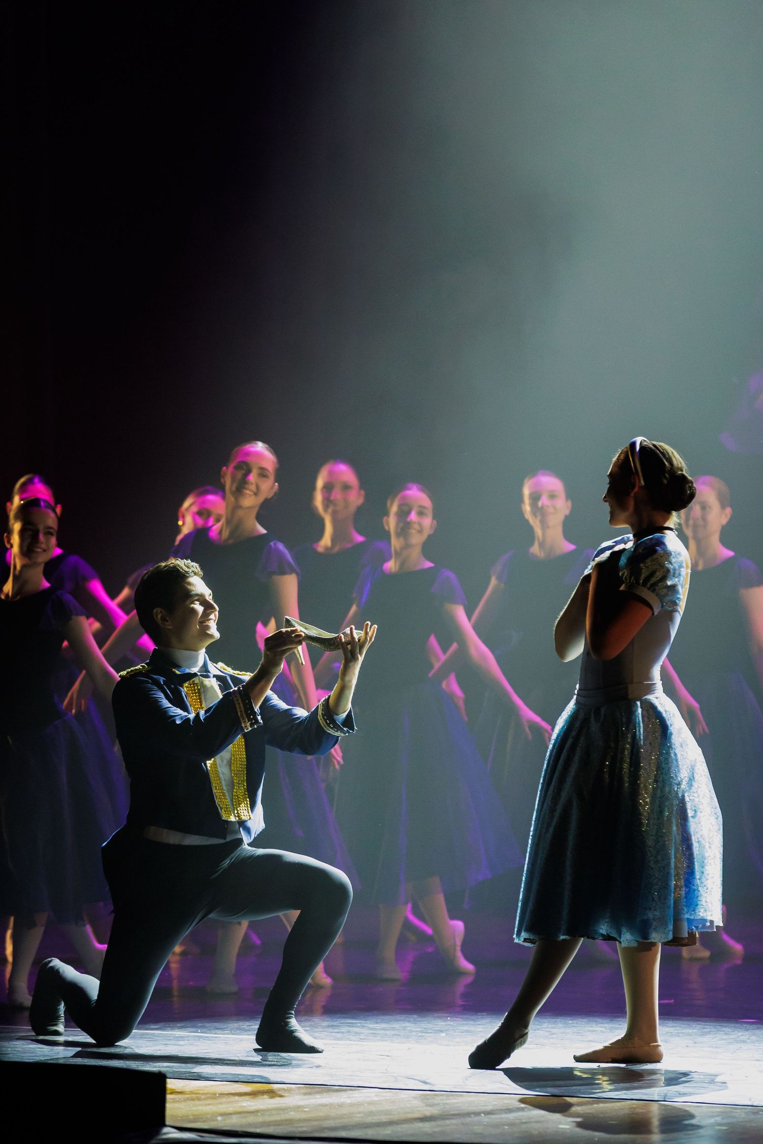 Elenco de teatro musical em cena sob iluminação de palco.