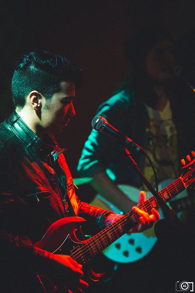 Guitarrista toca sob luzes vermelha e azul-turquesa.