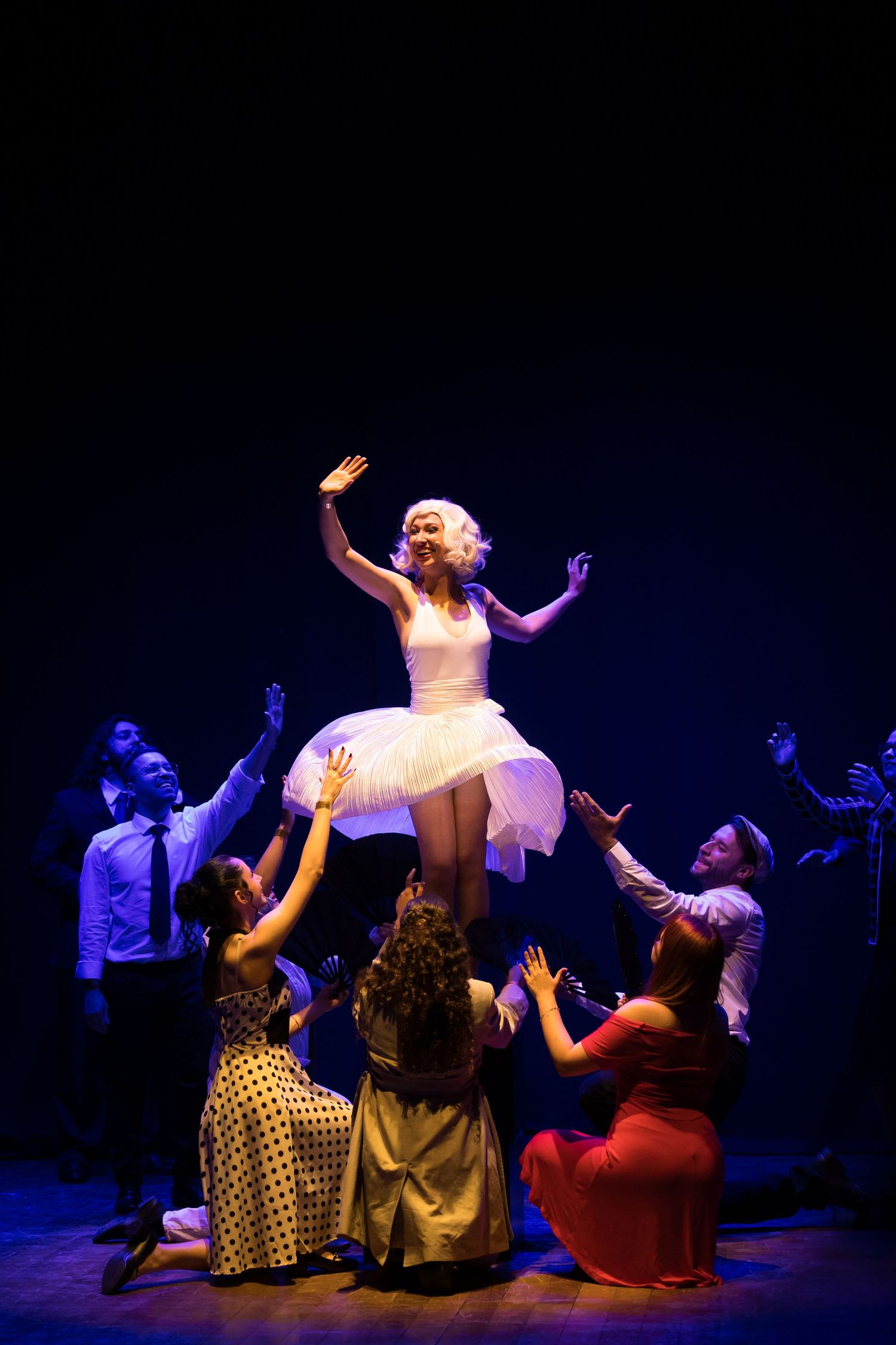 Atriz de vestido branco erguida pelo elenco no espetáculo Monroe.