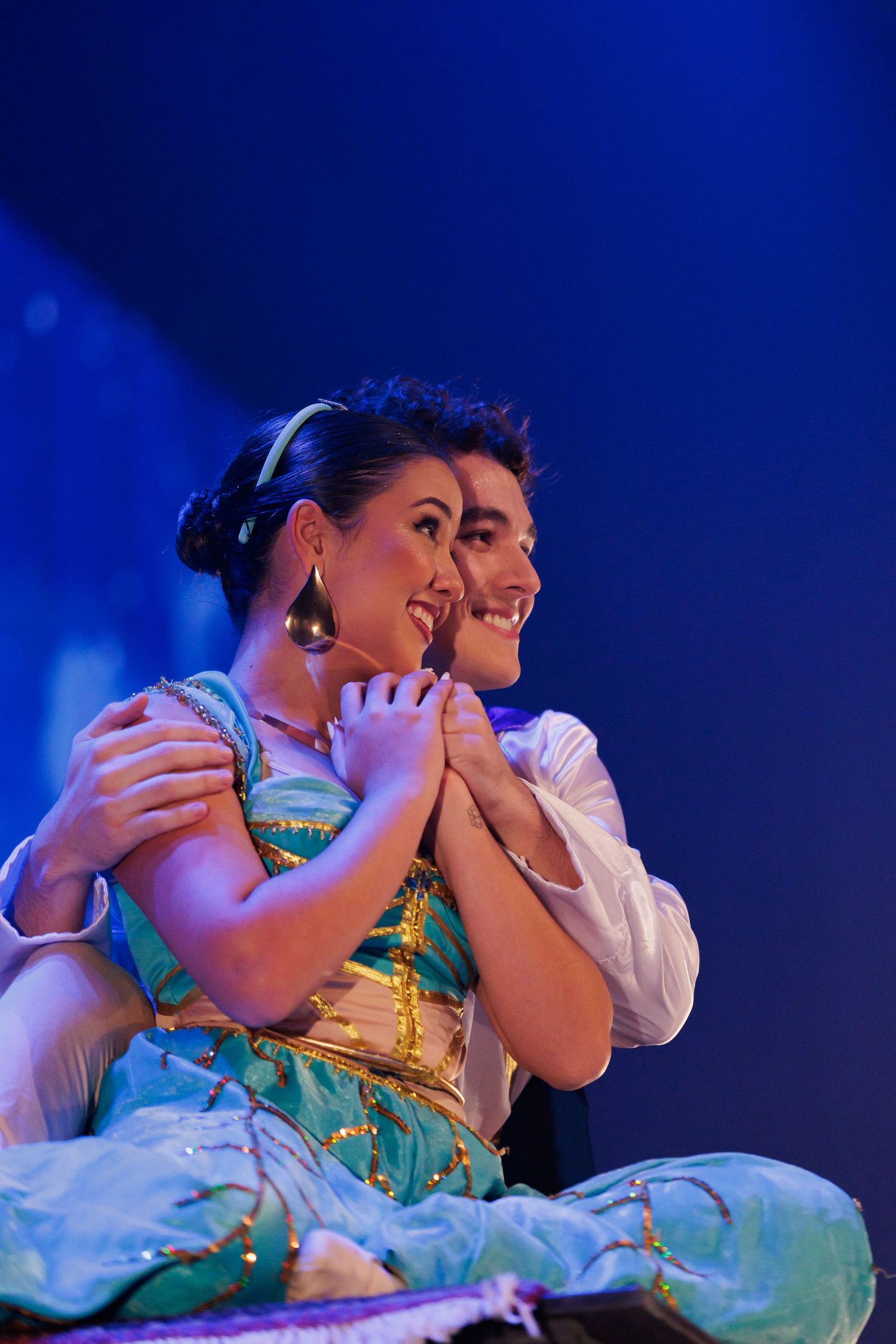 Dois atores em figurinos coloridos durante apresentação de teatro musical.