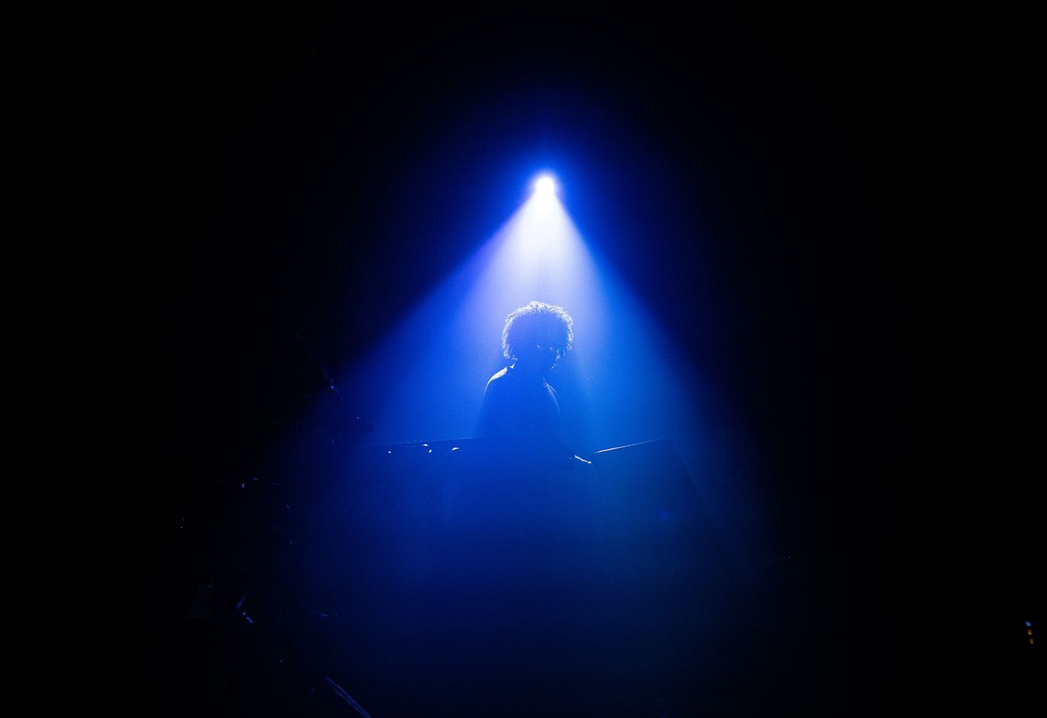 Silhueta de artista sob um foco de luz azul no palco.