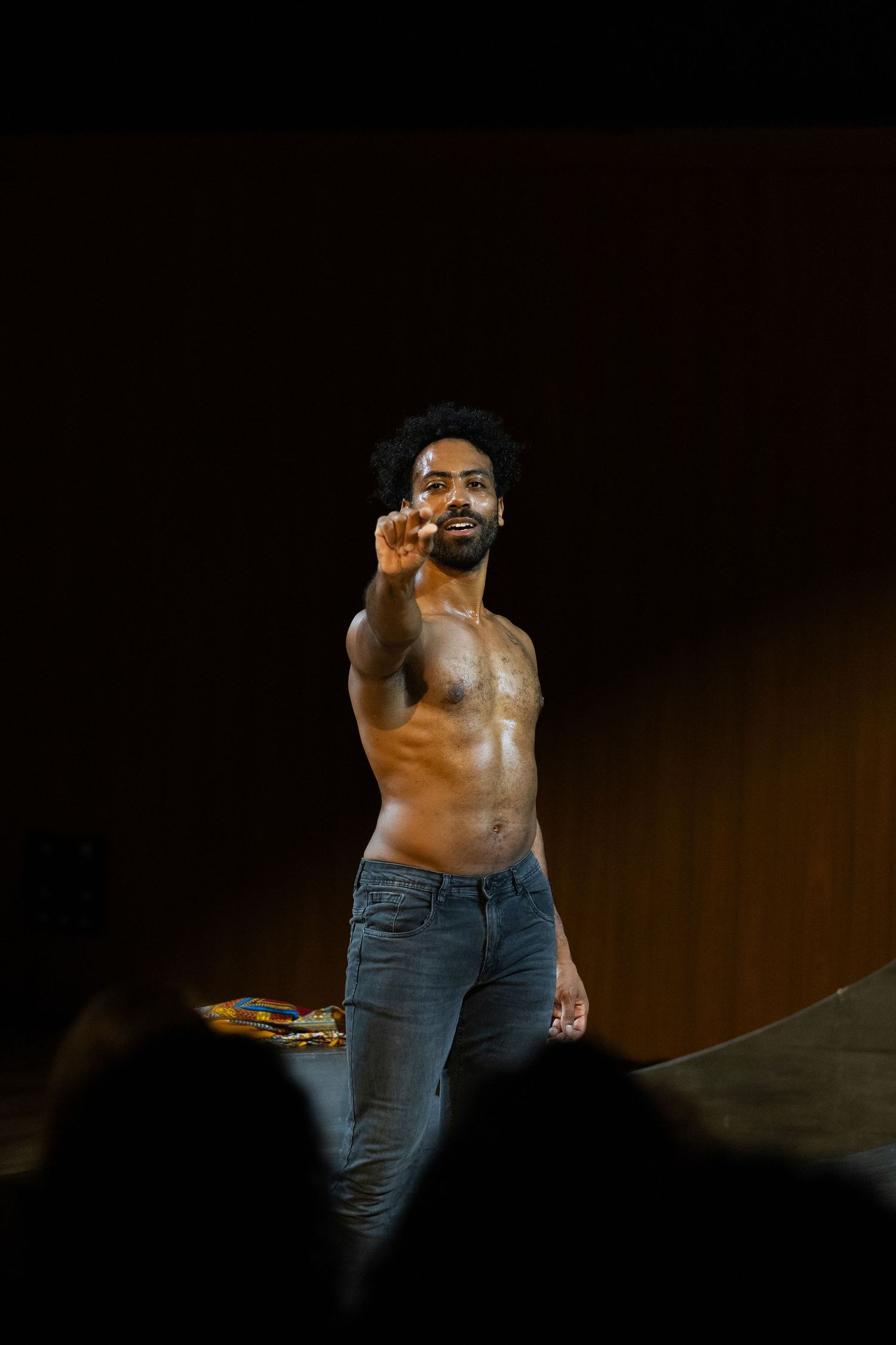 Intérprete sem camisa, de calça jeans, aponta para a plateia.