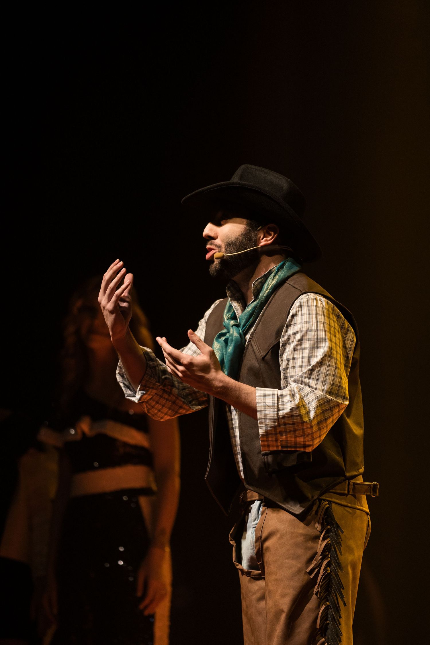 Intérprete de chapéu de cowboy ergue as mãos em cena, sob luz dourada.