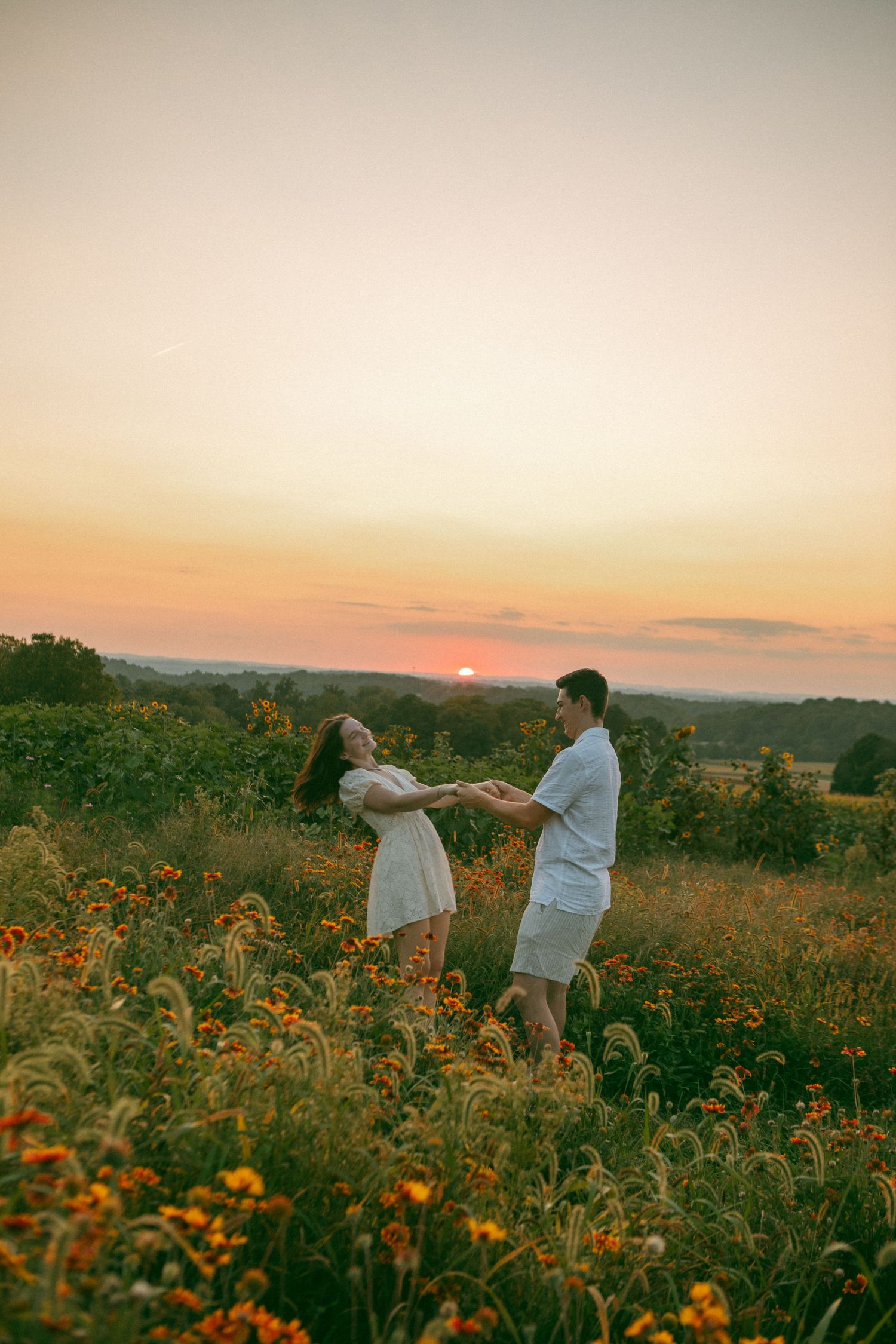 A couple dances joyfully in a wildflower field at sunset, embracing love and nature in a golden, romantic moment.