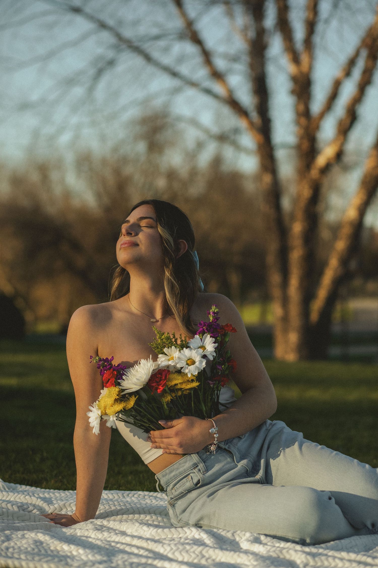 A woman basks in golden sunlight, embracing a bouquet of vibrant flowers, radiating peace and warmth in a serene outdoor setting.
